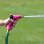 Hand holding a pink Sprout metal nozzle emitting a focused spray against a green lawn background