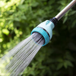 Close-up of Sprout watering wand nozzle spraying fine shower stream against blurred foliage