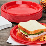 Stack of red disposable plates with a sandwich on a matching red plate on a wooden surface styled with napkins