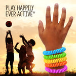 Stacked colorful coil bracelets shown on a raised child’s wrist silhouetted against a sunset with playful kids in the background.