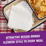 Stack of embossed white paper napkins on a tray next to a bowl of potato chips on a checkered cloth