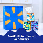 Three colorful Kleenex Anti‑Viral cube boxes stacked next to a blue and yellow reusable shopping bag on a kitchen counter, promotional copy below.