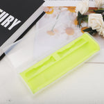 Open translucent toothbrush travel case with lime-green interior staged next to a book and white flowers on a textured surface.