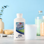 Stain Away Plus bottle next to a filled clear cup in a softly styled bathroom-themed scene