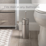 Vented stainless steel toilet brush holder positioned on a bathroom floor next to a toilet in a staged setting