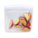 Clear Stasher silicone sandwich-style reusable bag filled with sliced peaches on a white background