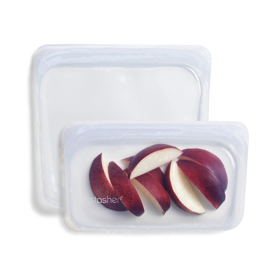 Two clear rectangular silicone Stasher bags stacked, front bag filled with sliced red fruit on white background