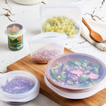 Kitchen counter with bowls and containers covered by clear Stasher silicone stretch lids and a can topped with a lid