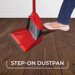 Person stepping on the red step-on dustpan as broom bristles sweep debris into the pan on a wood floor