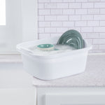 White Sterilite wash tub filled with soapy water and plates, placed on a kitchen counter near tiled backsplash