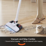 Person using white stick vacuum-mop on a wood floor with debris and a cat sitting nearby, showing vacuum head in use.