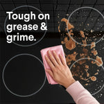 Hand wiping a stovetop with a pink cloth showing greasy residue and text 'Tough on grease & grime.'