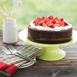 Layer cake topped with whipped cream and sliced strawberries on a green cake stand, styled with napkins and forks.