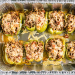 Baked stuffed green bell peppers arranged in an aluminum foil pan with melted cheese topping