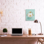 Lifestyle scene of a modern desk with a small teal canvas print of a gold toilet paper holder mounted on a white brick wall