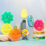 Styled scene of multiple Scrub Mommy smiley sponges and cleaning accessories arranged on a tiled surface