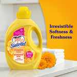 Suavitel yellow bottle on a counter beside folded towels and orange flowers with text ‘Irresistible Softness & Freshness’