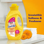 Suavitel yellow bottle on counter beside folded towels and flowers with text 'Irresistible Softness & Freshness'
