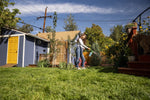 Wide lifestyle photo of a person watering a backyard garden while holding a blue Sunday WonderFert bottle with nozzle