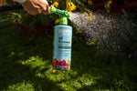 Action photo of a hand holding a Sunday WonderFert bottle with nozzle spraying water in a garden setting