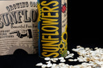 Close-up of sunflower seed kit tin next to packet-style instructions and scattered sunflower seeds on a dark surface.