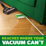 Swiffer mop reaching under a green couch beside a vacuum cleaner, illustrating access where vacuums can't reach