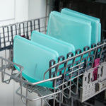Several teal silicone storage bags standing upright in a dishwasher rack to show they are dishwasher-safe