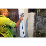 Person in a green shirt using a spray gun to apply a white coating to a concrete basement wall with visible mold stains