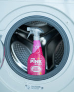 Pink The Pink Stuff spray bottle placed inside the drum of a front-loading washing machine, clear trigger visible