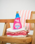 The Pink Stuff Miracle Laundry Sensitive detergent bottle sitting on folded pink and white towels on a wooden chair.