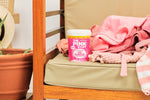The Pink Stuff Oxi Powder tub placed on an outdoor bench beside pink towels and clothing in a styled scene