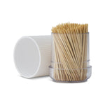 Clear plastic dispenser filled with natural bamboo toothpicks and a white ribbed cap resting beside it