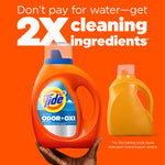 Hand holding a Tide Ultra Odor+Oxi bottle beside a generic yellow bottle with text about 2X cleaning ingredients