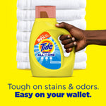 Hand holding a yellow Tide Simply All In One bottle against folded white towels on yellow background
