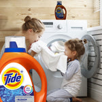 Large foreground Tide bottle with two children interacting near a front-load washer in a laundry room scene, Tide bottle repeated in background.