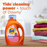 Tide Plus Downy April Fresh bottle on a wooden surface beside folded colorful clothes with cleaning power messaging