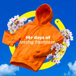Floating orange hoodie with blossoms and circular graphic reading '14+ days of lasting freshness' on blue sky background