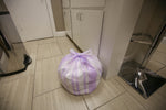 Tied lavender-and-white striped trash bag placed on a tiled floor near cabinets in a kitchen area