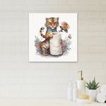 Square canvas wall art of a tiger holding a toilet-paper roll and roses, shown mounted on a light tiled bathroom wall above toiletries.