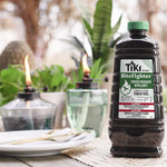 TIKI BiteFighter torch fuel bottle on a table with outdoor tiki torches and blurred plants in the background
