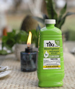 Green TIKI BiteFighter Clean Burn torch fuel bottle on a woven table with a lit torch blurred in the background