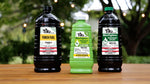 Three Tiki torch fuel bottles on a wooden surface outdoors, including a green BiteFighter bottle in the center
