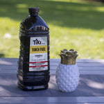Tiki citronella torch fuel bottle staged outdoors beside a decorative pineapple torch on a table