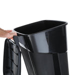 Hand holding the rear top edge while tilting a black plastic wheeled trash can, showing interior and lid.