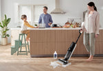 Kitchen scene with a person using a Tineco floor cleaner and a Tineco cleaning solution bottle on the floor beside a small spill