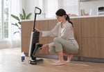 Woman kneeling to empty a Tineco floor machine bin with a Tineco cleaning solution bottle standing on the floor nearby