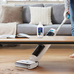 Tineco cleaning solution bottle placed on a coffee table while a Tineco floor machine cleans wood floor in a living room scene