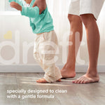 Close crop of toddler taking first steps helped by adult legs, large translucent Dreft logo overlaid