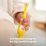 Close-up lifestyle image of a toddler holding a yellow Frida Baby toothbrush with suction-cup base