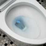 Top-down view of a toilet bowl with a dissolving blue cleaning pod releasing blue specks into the water